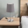 A bedside lamp sits on a wooden nightstand next to a bed. Náhled obrázku produktu