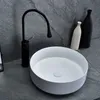 A modern bathroom sink with a black faucet and decorative vases in the background. Anteprima dell’immagine prodotto