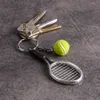 A set of keys with a tennis racket and ball keychain attached, resting on a dark gray surface. Náhled obrázku produktu