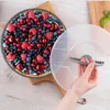 A hand is shown holding the lid of a round cake pan filled with berries, placed on a wooden board. Náhľad obrázku produktu