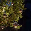 Several solar-powered lanterns hang from tree branches at night. Produktbild-Vorschau