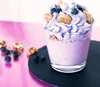 A close-up of a blueberry dessert in a glass, with blueberries and cookies scattered around. Produktbild-Vorschau