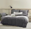 A neatly made bed with gray bedding and pillows, a chair, and a lamp in the background. Podgląd zdjęcia produktu