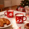 A festive Christmas breakfast scene with steaming mugs of hot chocolate, croissants, sausages, and a decorated Christmas tree in the background. Produktbild-Vorschau