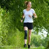 A woman is running on a path surrounded by greenery. Produktbild-Vorschau