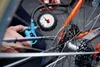 A close-up shot of a person using a bicycle tire pressure gauge on a bicycle wheel. Náhľad obrázku produktu