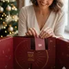 A woman is opening an advent calendar with a Christmas tree in the background. Produktbild-Vorschau