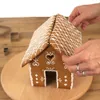Hands assembling a gingerbread house on a wooden board. Voir les images du produit