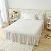 A white bed with a ruffled bed skirt and pillows, set against a white headboard and wall. Produktbild-Vorschau