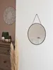 A round mirror with a black frame hangs on a textured white wall. To the left, on a wooden dresser, are two decorative vases with gold and green accents, and a large dried pampas grass plume stands in the foreground. Produktbild-Vorschau