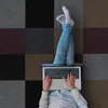 A person is lying on a floor with a laptop on their lap, their legs are propped up on the laptop. Náhled obrázku produktu