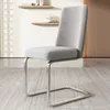 A gray upholstered dining chair with silver metal legs is shown in a room with a tiled wall and wooden door. Náhľad obrázku produktu
