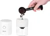 A hand is pouring coffee beans into a coffee grinder. A separate part of the coffee grinder is shown to the left. Podgląd zdjęcia produktu