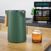 A green electric kettle with a wooden handle is shown on a kitchen counter next to a glass mug of tea. The background shows a modern kitchen setting. Podgląd zdjęcia produktu