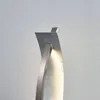 A close-up of a modern, silver-colored LED table lamp with a curved design, mounted against a textured light gray wall. Produktbild-Vorschau