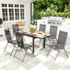 An outdoor dining set with a table and chairs on a patio, with a grill in the background. Produktbild-Vorschau