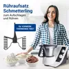 A woman is smiling and leaning on a kitchen counter next to a food processor. In front of the processor are three bowls of whipped cream and chocolate cream. A whisk attachment is shown to the left. Produktbild-Vorschau