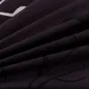 A close-up view of black fabric with a white leaf pattern, showing the texture and folds of the material. Náhled obrázku produktu