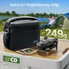 A drone and its carrying case are displayed on a table outdoors, with a tent and a person relaxing in the background. Produktbild-Vorschau