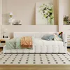 A bedroom scene featuring a white daybed with several pillows and blankets, a painting on the wall, and decorative items on a shelf. Voir les images du produit