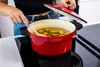 A person is cooking potatoes in a red pot on a stovetop. Podgląd zdjęcia produktu