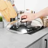 A hand is placing a glass lid on a gas stove in a kitchen. Podgląd zdjęcia produktu