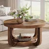 A round wooden coffee table with a two-tiered shelf, decorated with a vase of flowers and books, in a living room setting. Anteprima dell’immagine prodotto