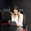 A woman wearing headphones is sitting at a desk in a recording studio, looking at a clipboard and smiling. Produktbild-Vorschau