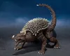 A toy figure of a dinosaur-like monster with spikes on its back and tail, standing on a dark surface against a blue, cloudy background. Náhled obrázku produktu