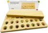 A wooden board game with colorful stones in its pits, with its packaging in the background. Produktbild-Vorschau