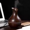 A dark wood-grain aroma diffuser is shown on a desk next to a laptop and a phone. Produktbild-Vorschau