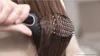 A close-up shot of a person using a black and pink electric hair straightening brush on their brown hair. Produktbild-Vorschau