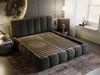 A modern bedroom with a large, upholstered bed as the focal point. The room features a large moon-like art piece on the wall, a bedside table with decor, and a window with sheer curtains. Produktbild-Vorschau