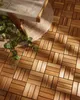 A close-up view of wooden deck tiles on a patio, with a plant and a section of a bench visible. Náhled obrázku produktu