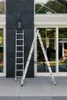 Two ladders are placed on a paved surface in front of a modern building with large windows. Produktbild-Vorschau