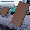 A brown leather phone case is shown in a close-up, angled view against a textured, cracked ground background. In the background, a green industrial vehicle is partially visible. Anteprima dell’immagine prodotto