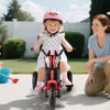 A young child is riding a red tricycle in a backyard, with an adult kneeling beside them. Náhled obrázku produktu
