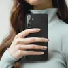 A person holding a black smartphone with a protective glass cover on the camera lens. Produktbild-Vorschau