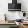A modern kitchen scene featuring a black range hood above an induction cooktop, with a hand holding a smartphone controlling the appliances. Náhled obrázku produktu
