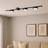 A black track light fixture with three adjustable spotlights is mounted on a light gray ceiling above a sofa with two framed pictures on the wall. Produktbild-Vorschau