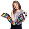 A young girl is holding a rainbow-colored, flexible keyboard. The keyboard is unrolled and curved, with the girl holding one end in each hand. She is smiling at the camera. Produktbild-Vorschau