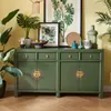 A green sideboard with drawers and cabinets, decorated with plants and artwork, in a room with yellow walls and a wooden floor. Voir les images du produit