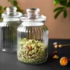 Two glass jars with lids, one filled with dried herbs or potpourri, are placed on a dark surface with some dried flowers in the foreground. Produktbild-Vorschau