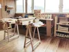 A woodworking workshop with sawhorses holding lumber, tools on a wall, and shelves with supplies. Anteprima dell’immagine prodotto