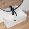 A rectangular white sink with a black faucet is shown on a wooden floor, with a round mirror reflecting the sink and faucet. Anteprima dell’immagine prodotto