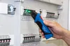 A hand is holding a voltage tester and checking a circuit breaker panel. Náhľad obrázku produktu