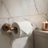 A toilet paper holder with a roll of toilet paper and a lit candle on a toilet tank, set against a marble wall. Anteprima dell’immagine prodotto
