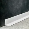 A white L-shaped profile strip is shown along the base of a dark, textured wall and a grey tiled floor. Anteprima dell’immagine prodotto