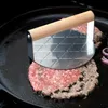 A burger press is being used to flatten raw burger patties in a cast iron skillet. Náhled obrázku produktu