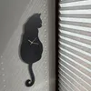 A black cat-shaped clock is mounted on a wall, with light filtering through blinds. Produktbild-Vorschau